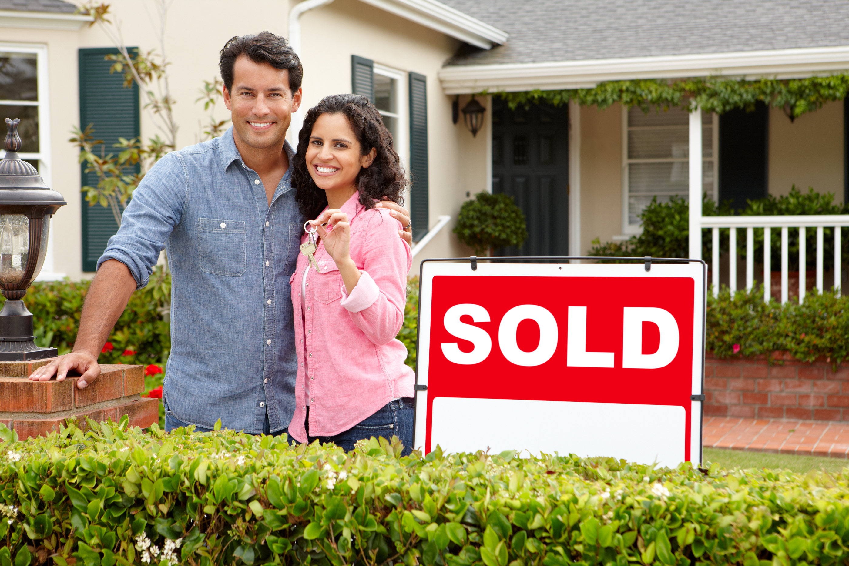 Hispanic couple outside home with sold sign